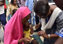 Le Représentant de l’OMS au Burkina Faso, Dr Alimata J. DIARRA-NAMA aidant une mère à administrer une dose de médicament de chimio prévention du paludisme à son enfant 