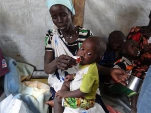 Woman giving PlumpyNut nutritional aid to her children in former Unity State