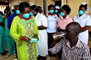 A TB patient receives treatment drugs from the Minister of Health on Sarah Opendi as other health workers look on 