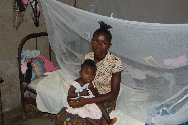 A mother and child seated on a bed with an insecticide treated bed ne