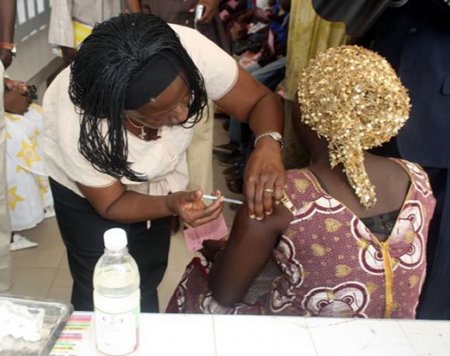 Le Représentant de l’OMS administrant une dose de vaccin à une jeune femme au poste de santé de Léona