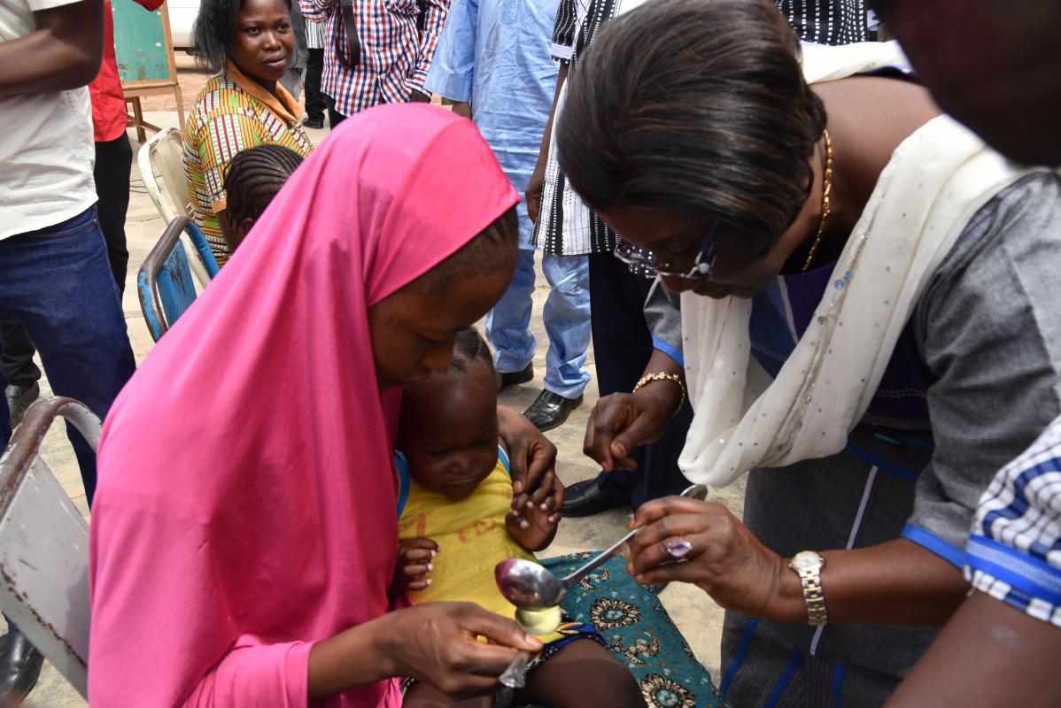 Le Représentant de l’OMS au Burkina Faso, Dr Alimata J. DIARRA-NAMA aidant une mère à administrer une dose de médicament de chimio prévention du paludisme à son enfant 