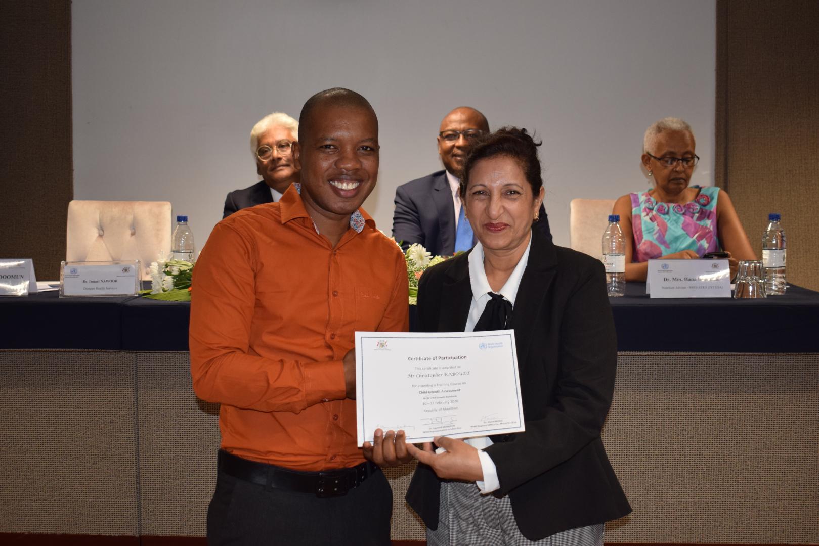 Mr Christopher Raboude, Nutritionist, Rodrigues Island, receiving the Certificate of Participation from Mrs Aryamah Doomun, Chief Nutritionist.  In the background, Dr I. Nawoor, Ag Director Health Services, Dr L. Musango, WHO Representative in Mauritius and Dr H. Bekele, Nutrition Advisor, WHO IST/ESA