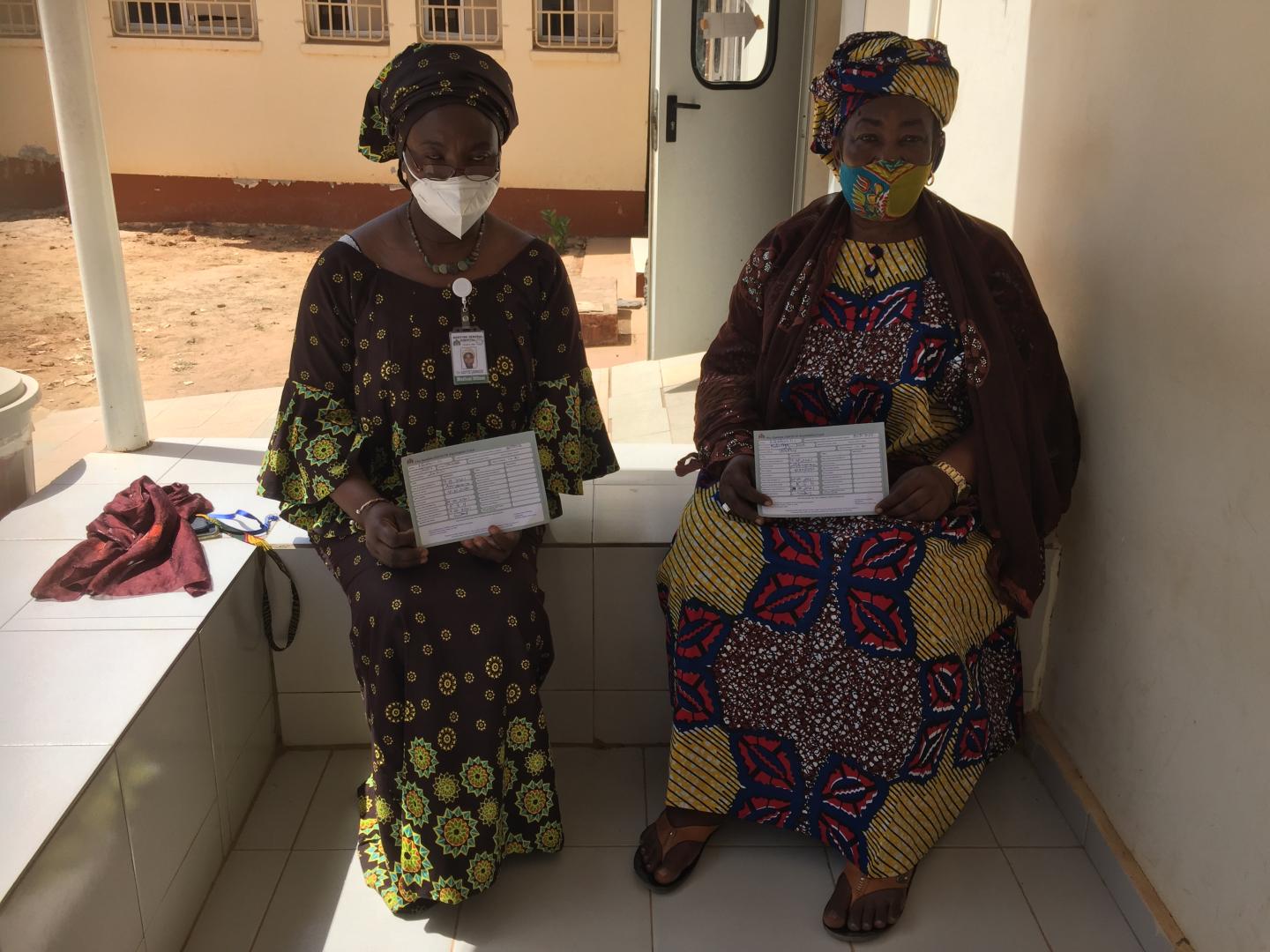 Madame Amie Jobe and one of her daughters, a medical Doctor, diplaying their vaccination cards, after receiving the COVAX vaccine