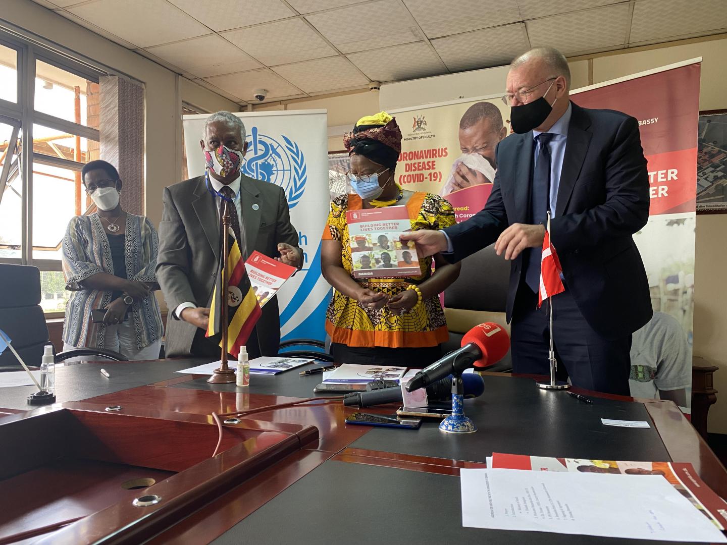 WHO Representative in Uganda, Dr Yonas Tegegn Woldemariam (white shirt) and Mr. Henrik Jespersen, the Head of Cooperation, Royal Danish Embassy in Kampala exchange signed agreements as Hon Hanifa Kawooya (yellow) and Dr Diana Atwine (white and black) look on at the Ministry of Health headquarters in Kampala