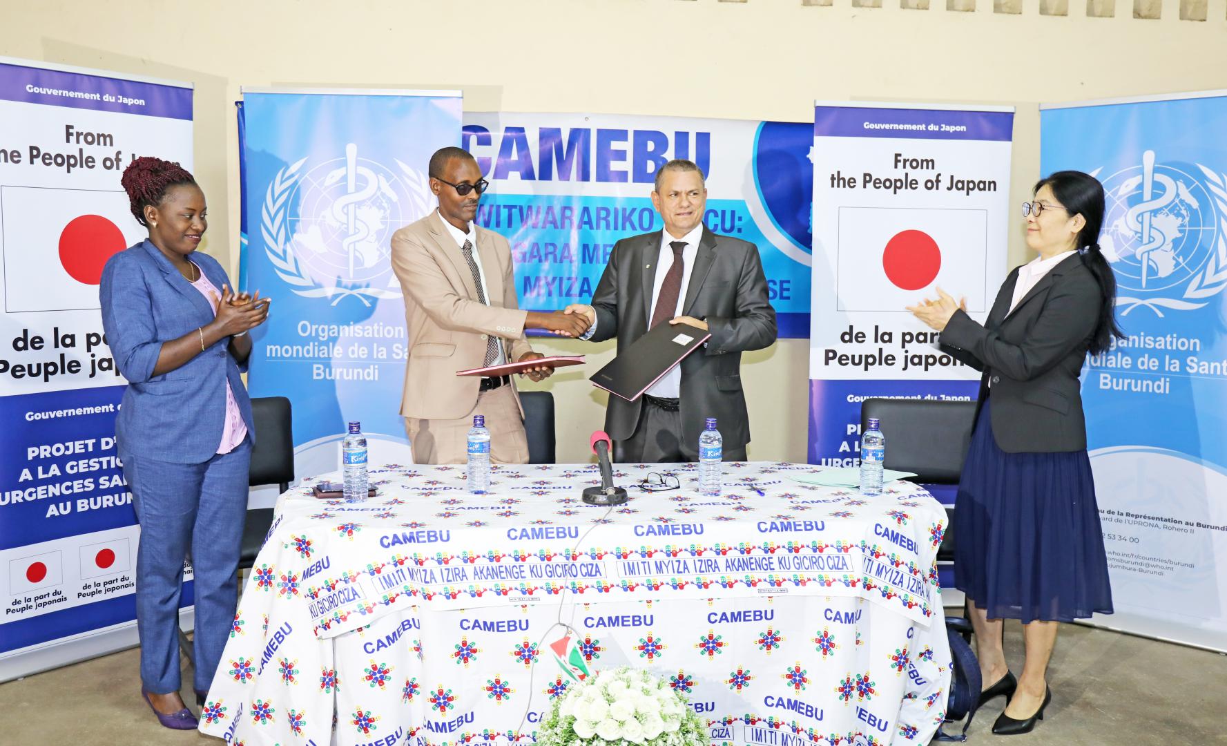 Le Représentant de l’OMS Burundi et l’Assistant au Ministère de la santé publique et de la lutte contre le Sida échangeant les documents de remise et réception des médicaments. A leurs côtés, la	Représentante de l’Ambassade du Japon (à gauche) et la Directrice Générale de la CAMEBU (à droite).