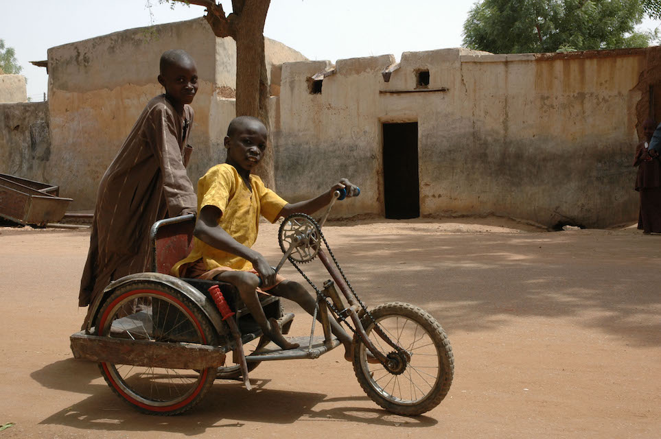 A young polio survivor with a friend on his  hand-operated tricycle in Kano State, Nigeria © Christine McNab