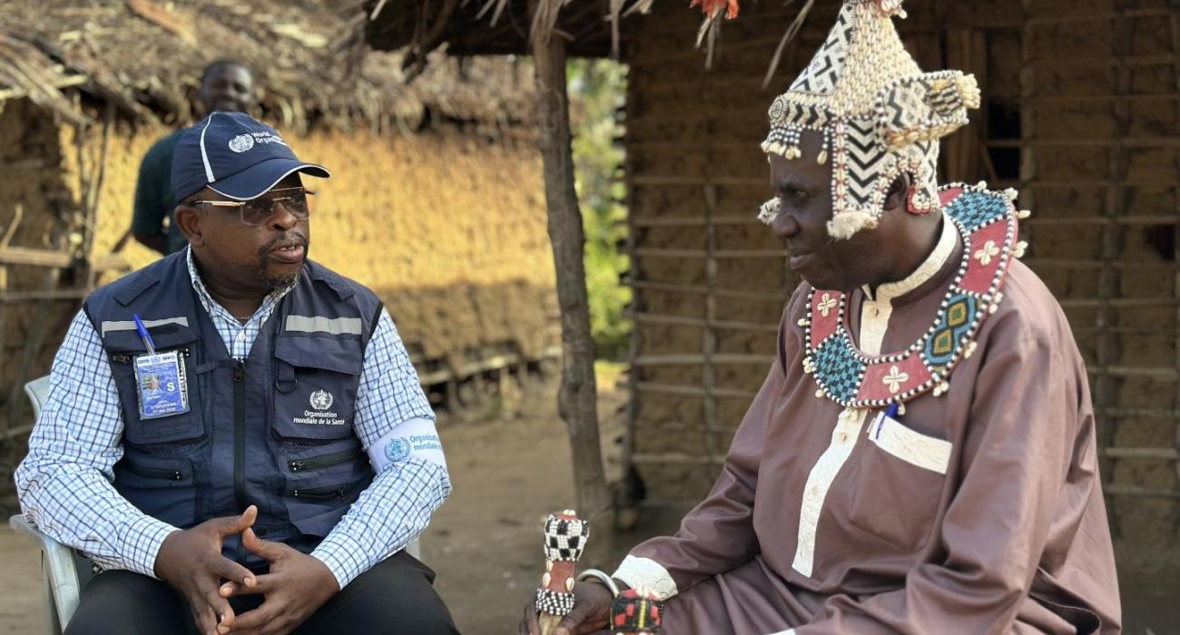Dr John Otshudiema, épidémiologiste et gestionnaire adjoint de l’incident Ebola pour l’OMS, échange avec le chef coutumier Bidiaka. Ce dernier lui explique comment les rites ancestraux ont contribué à accélérer le contrôle de la maladie à virus Ebola dans la zone de santé de Bulape. Crédit photo : OMS/René Ifono