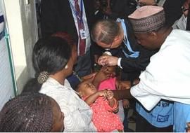 Assisted by the Executive Director of the NPHCDA Dr Ado Muhammad, UN Secretary General administers oral polio vaccine to a child in a WHO supported health facility