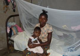 A mother and child seated on a bed with an insecticide treated bed ne