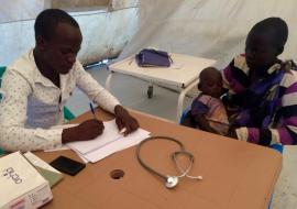 The "EWARS in a box" kit is designed with frontline health care providers in mind. Here Julius Opio, Clinical Officer in-charge with Health Link South Sudan, sees patients in Site 1 Health Facility in Mingkaman, South Sudan. Julius collects disease data from patients each day during routine consultations. If any diseases with immediate reporting requirements are seen, these can be notified immediately to the County Health Department using a mobile phone