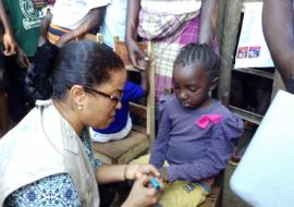 Representante da OMS marcando o dedo da criança vacinada