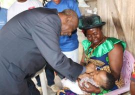 Le Secrétaire d’Etat à la Santé Publique Chargé de la Lutte contre les Epidémies et les Pandémies administre le vaccin polio oral à un nourrisson porté par sa grand-mère.