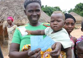 A woman and her child in Yendeya Village displaying her child's measles vaccination card. Photo credit: WHO/S. Gborie