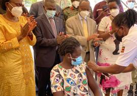 Ministry of Health leadership and partners led by the Minister of Health Hon Dr Jane Ruth Achieng (yellow) observe as a community member receives her COVID-19 vaccine shot at the launch in Moroto District. ©WHOUganda