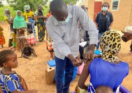 A man vaccinating a woman carrying a baby on her back