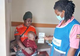 A Health worker hands over a child immunization card to a mother