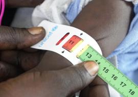 A health worker checks the circumference of a child's arm using a mid-upper arm circumference measure