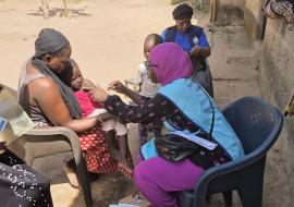 A mother holds her child as a health worker delivers a life-saving measles-rubella vaccine in Cape Point, The Gambia.