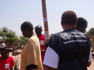 Community drug distributors and WHO staff with poles they use to measure the height of participants during a mass drug administration. Height is used to determine the proper treatment dosage for participants. e.g. an individual who is above 158 cm, which has the number 4, would receive four doses of ivermectin