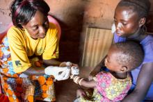 Pascaline, a volunteer relais communautaire, gently pricks Elessa's finger to draw blood for the rapid diagnostic test that will determine whether Elessa has malaria.