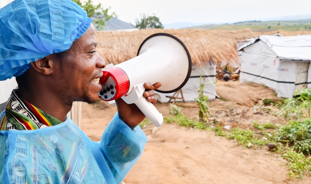 Gilbert Djuma Kamona, crieur et relais communautaire du site de Kisalaba, en train de sensibiliser les habitants déplacés internes pour se faire vacciner et se protéger de la COVID-19 