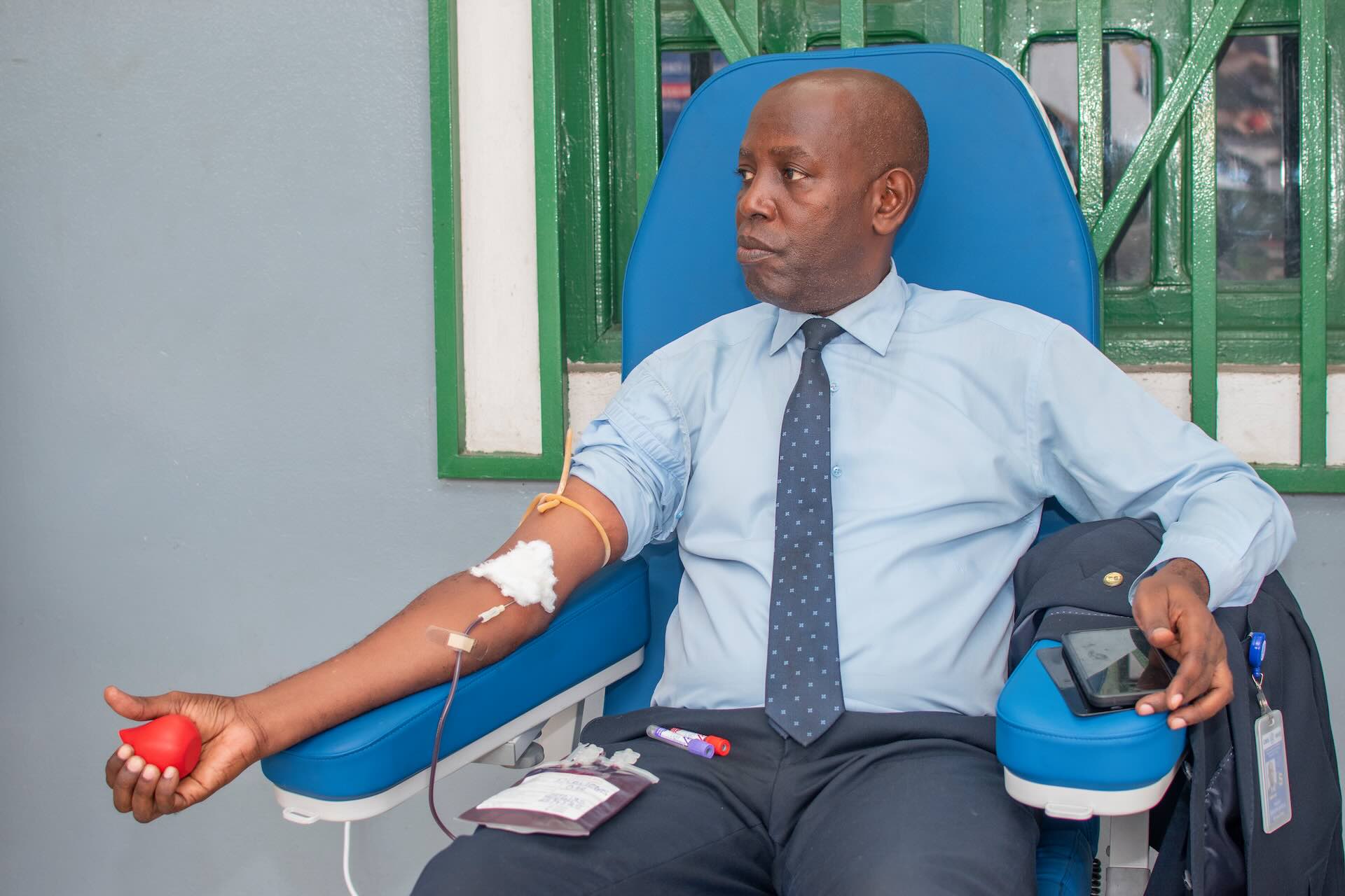A donor in shirt and tie giving blood, holding a heart-shaped stress ball